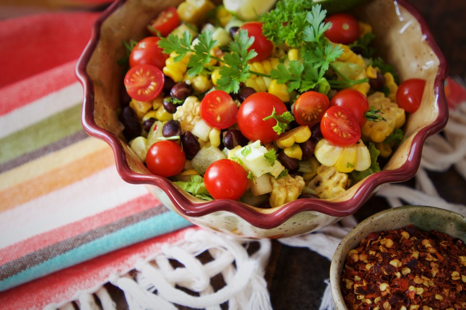 Tigela de salada colorida com tomate, milho e feijão preto sobre toalha listrada